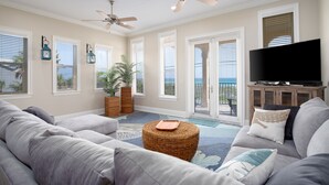 A living room with a sofa, a television, and a view of the ocean through large windows.