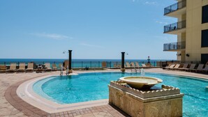 A pool area with a hot tub, lounge chairs, and a view of the ocean.