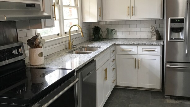 Uma cozinha moderna com armários brancos, eletrodomésticos de aço inoxidável e bancada de granito.