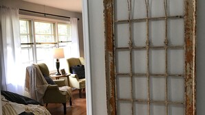 Quarto com uma grande janela em arco, piso de madeira, cama, cadeira e mesa com abajur.