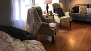 Um quarto aconchegante com uma cama, uma poltrona, uma mesinha com abajur e um sofá.