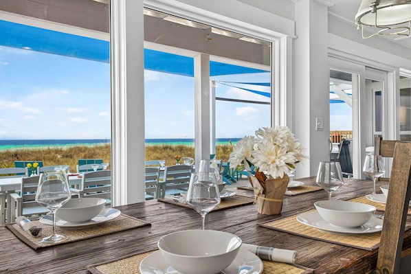 A dining table set with white bowls and wine glasses, overlooking a beach view.