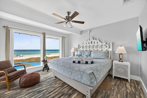 A bedroom with a large bed, a ceiling fan, a view of the beach, a chair, and a nightstand with a lamp. - Luxury Gulf Front Property! Directly on the Beach! Sleeps 15! (Panama City Beach)