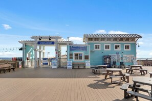 Un muelle con un edificio azul, mesas de picnic y un cartel que indica Playa Panama City.