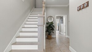 Un escalier avec des marches blanches et des rampes en bois, menant à un palier où se trouve un pot de fleurs.