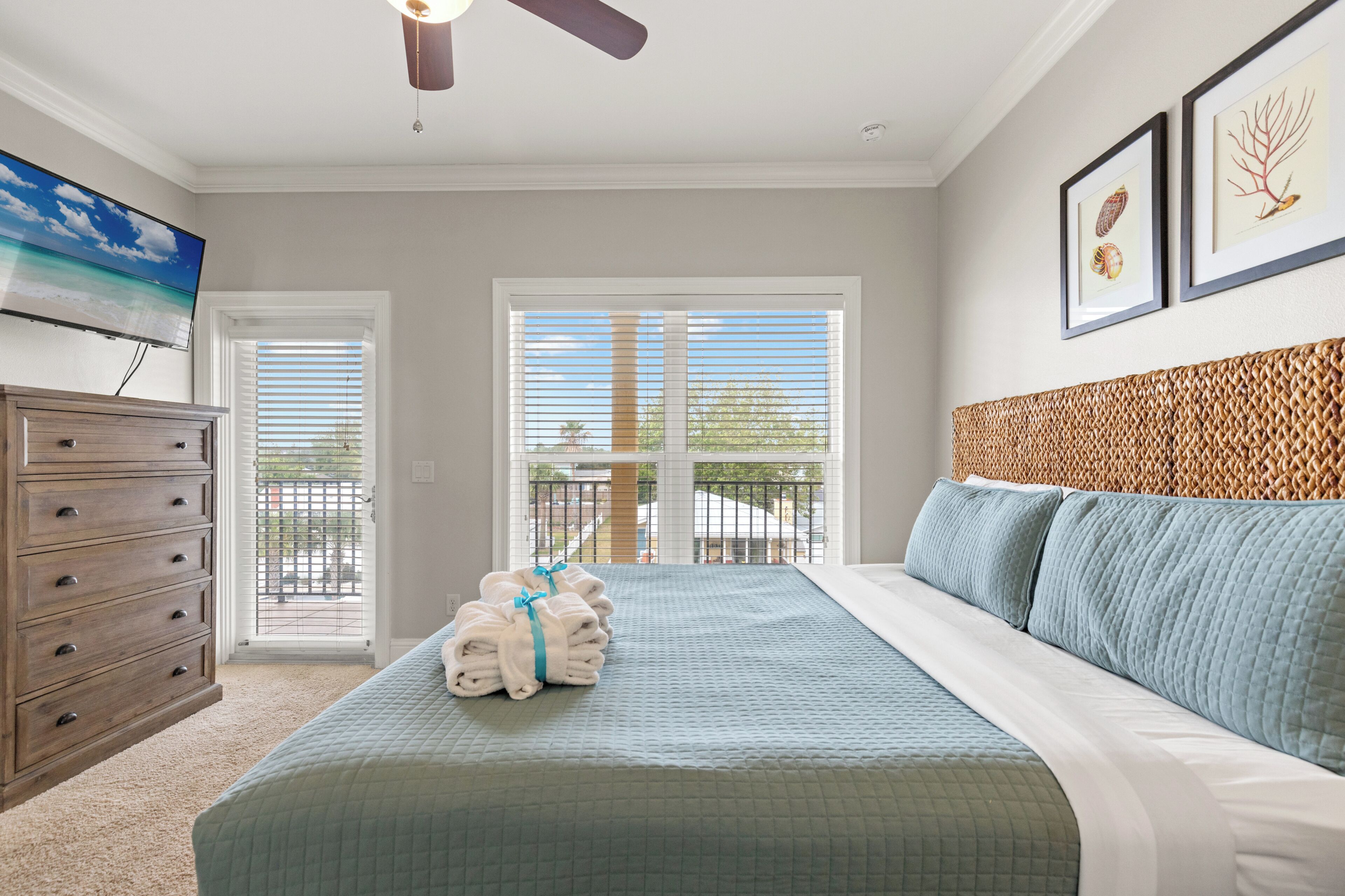 A bedroom with a bed, a dresser, a ceiling fan, a TV, and a balcony with a view.