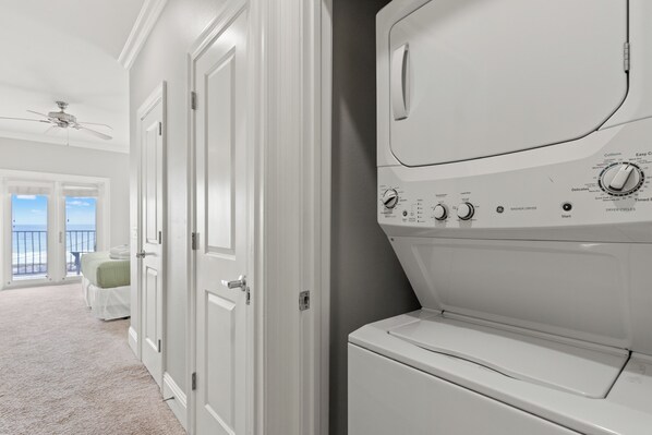 A laundry room with a front-loading washer and dryer, a ceiling fan, and a view of the ocean through large windows. - Walk To The Beach! 3 Story Home! 2 Balconies With Gulf Views! (Panama City Beach)