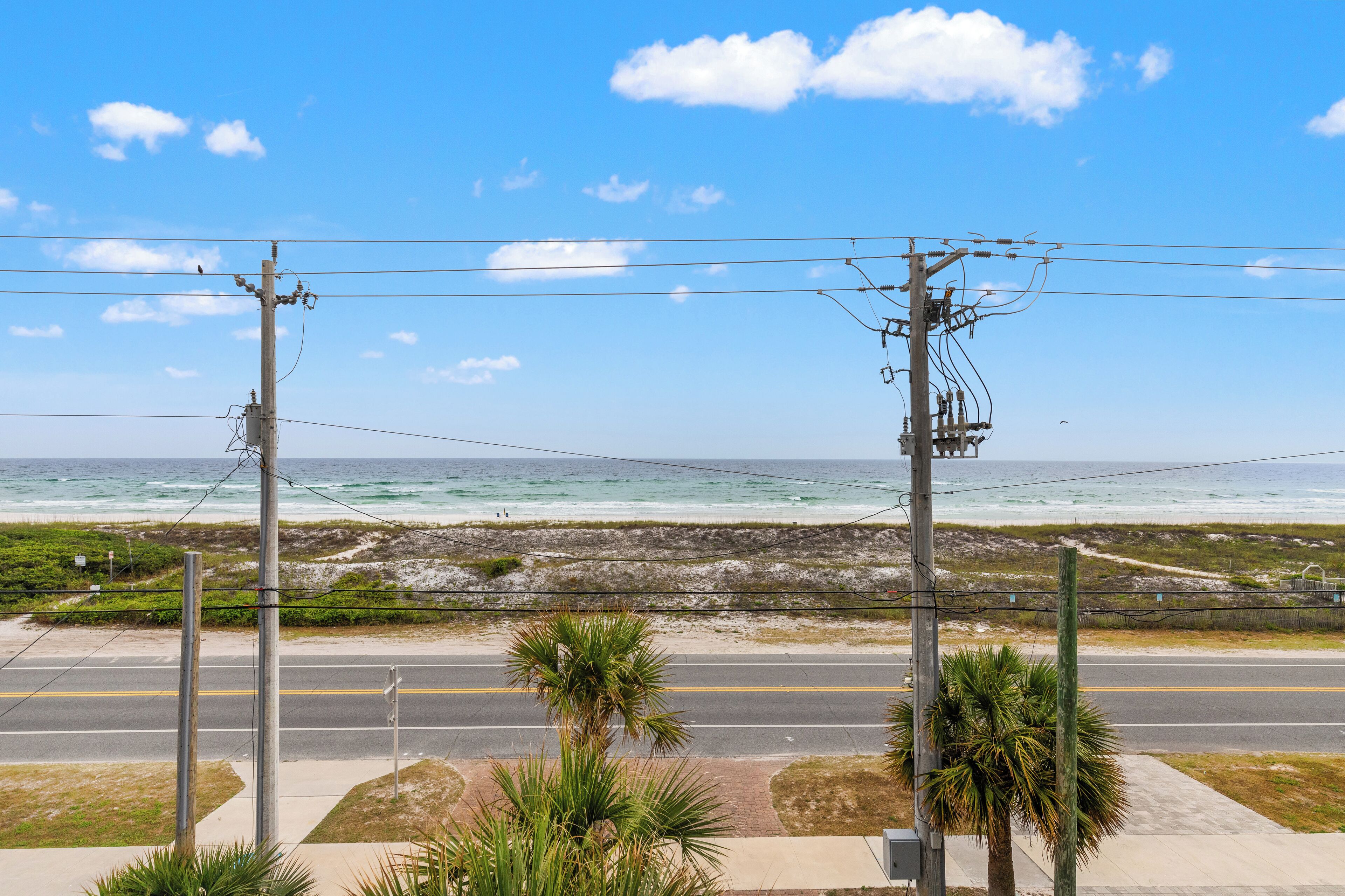 A coastal road with power lines and a beach in the background.