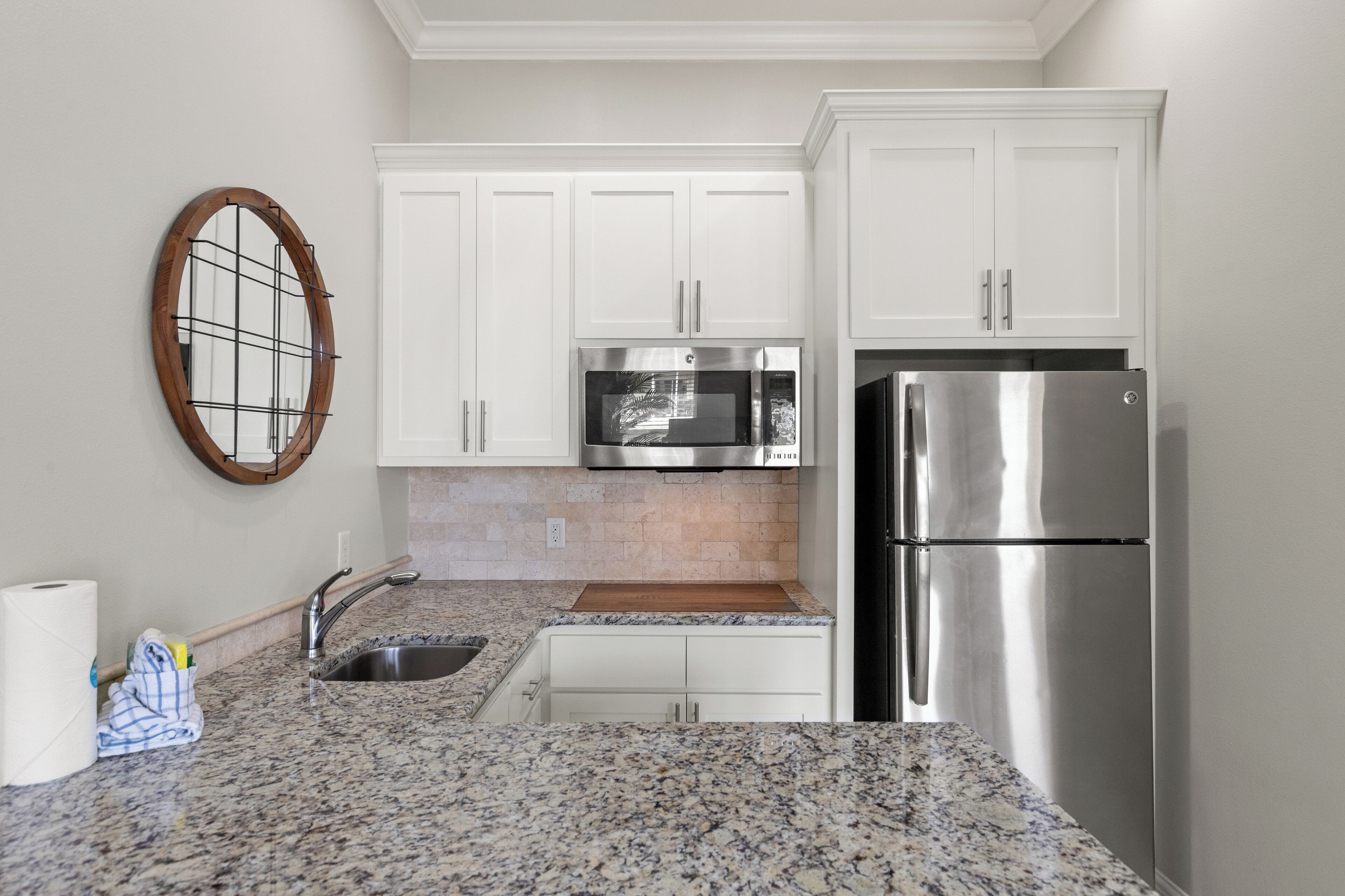 A kitchen with white cabinets, a stainless steel refrigerator, a microwave, and granite countertops.