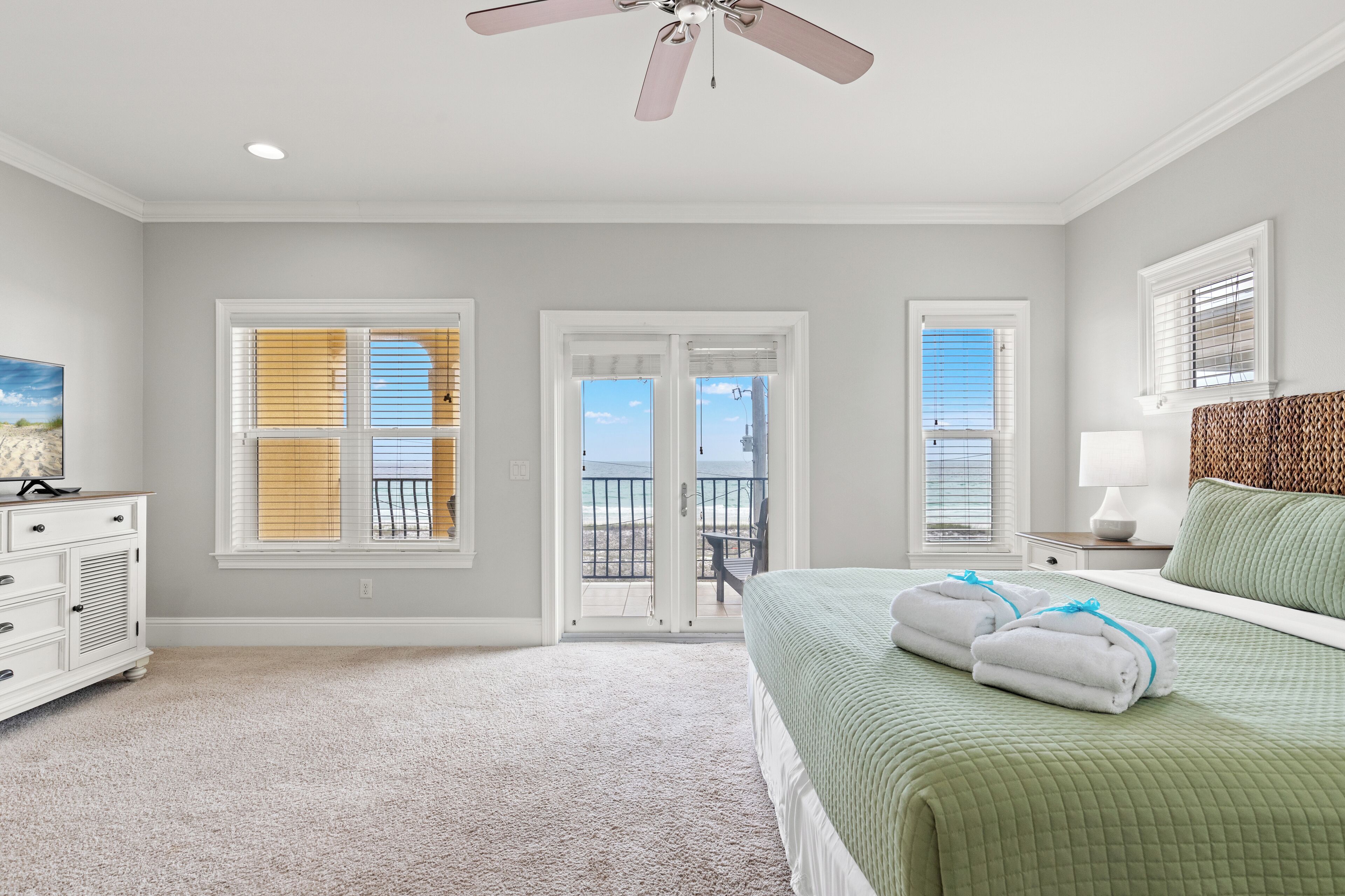 Une chambre à coucher comprenant un lit, une commode, un ventilateur de plafond et un balcon avec vue sur l’océan.