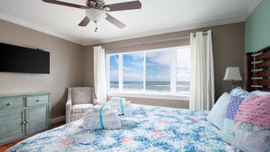 Une chambre à coucher comprenant un lit, une chaise, une table de chevet, une fenêtre donnant sur l’océan et un ventilateur de plafond.