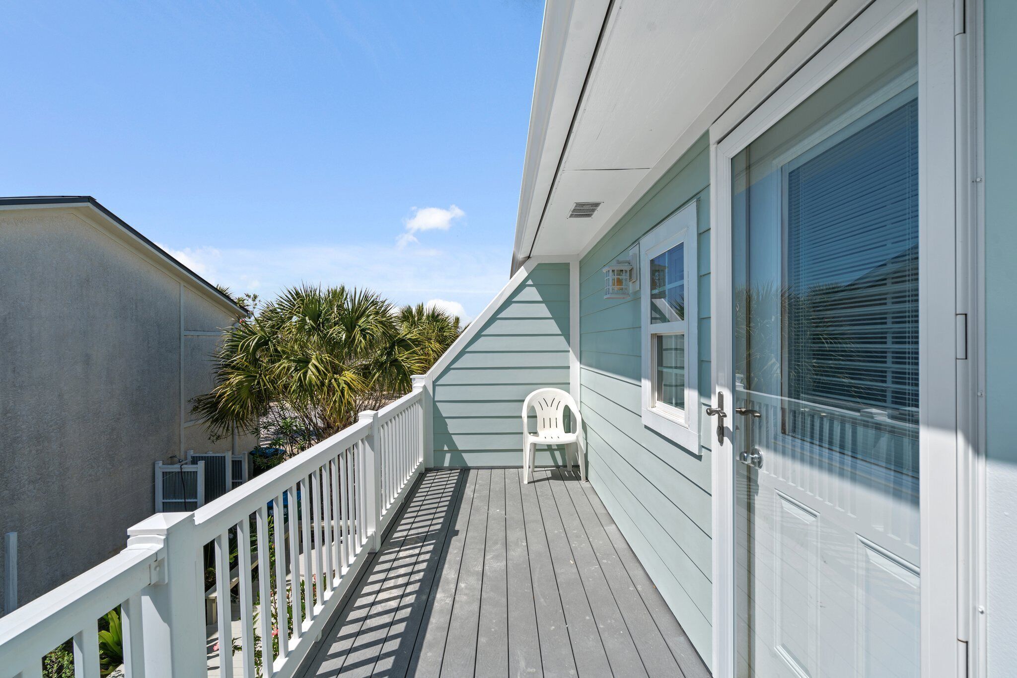 A wooden deck with a white railing, a white plastic chair, and a door with a window.