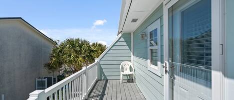 A wooden deck with a white railing, a white plastic chair, and a door with a window.