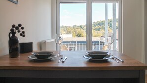 Une table à manger avec deux bols et des couverts, un vase, et une fenêtre donnant sur un bâtiment et des arbres.