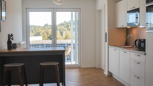 Une cuisine moderne avec des meubles blancs, un plan de travail en bois et une vue sur un balcon donnant sur le paysage urbain.