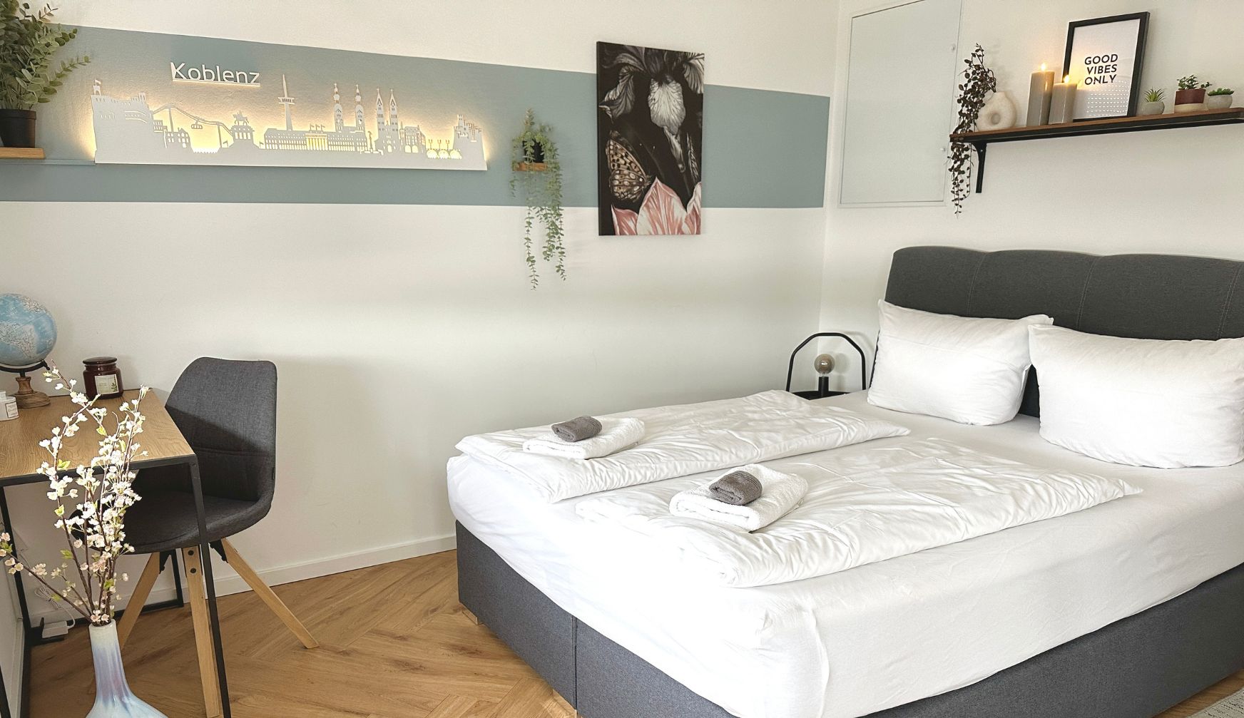 Ein modernes Hotelzimmer mit einem großen Bett, einem Schreibtisch mit Stuhl, einem Globus und einem Stadtbild an der Wand.