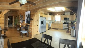 Interior de una cabaña de madera con sala de estar, cocina y escalera.