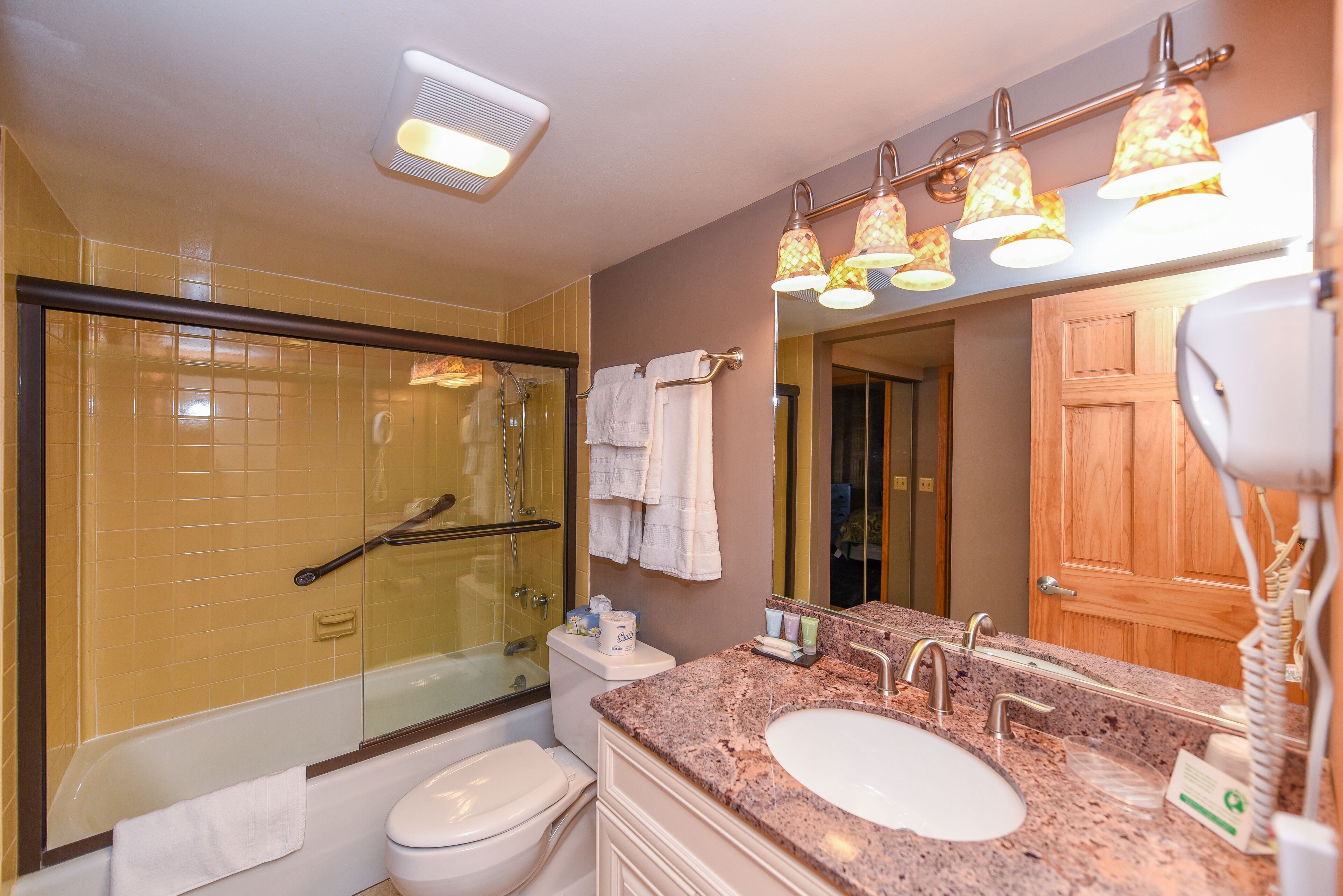 Une salle de bain dotée d’une douche à parois de verre, de toilettes blanches, d’un lavabo avec un meuble-vasque et d’un miroir au-dessus du lavabo.