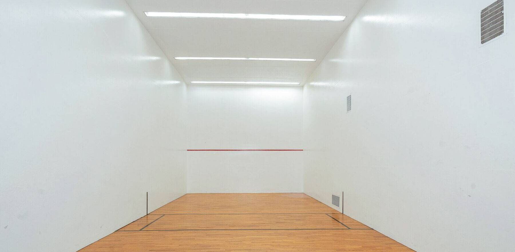 Ein Squashplatz mit weißen Wänden, einem Holzboden und Neonbeleuchtung.