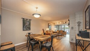 Una sala de estar moderna con comedor, que incluye una mesa y sillas de madera, un sofá y un televisor sobre un mueble.