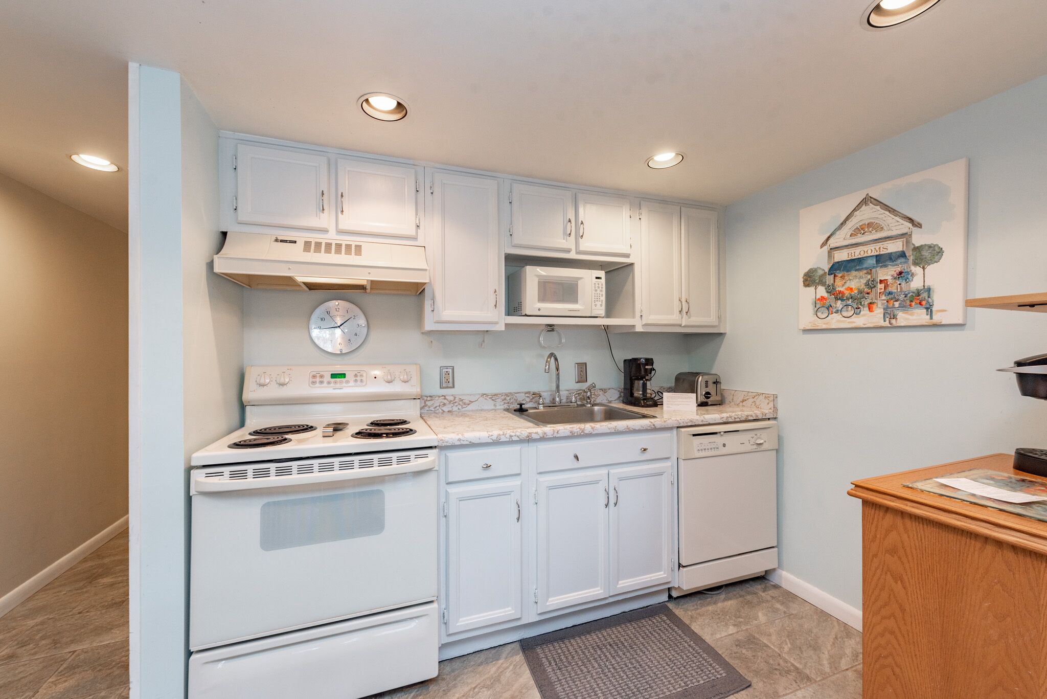 A kitchen with white cabinets, a microwave, a stove, a sink, and a clock.