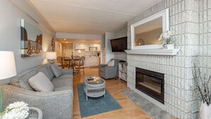 Un salon avec une cheminée, un canapé, une table basse et, au fond, un coin repas.