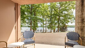 Une terrasse avec deux chaises à motifs et une petite table, donnant sur un lac où l’on peut voir des bateaux et des arbres.