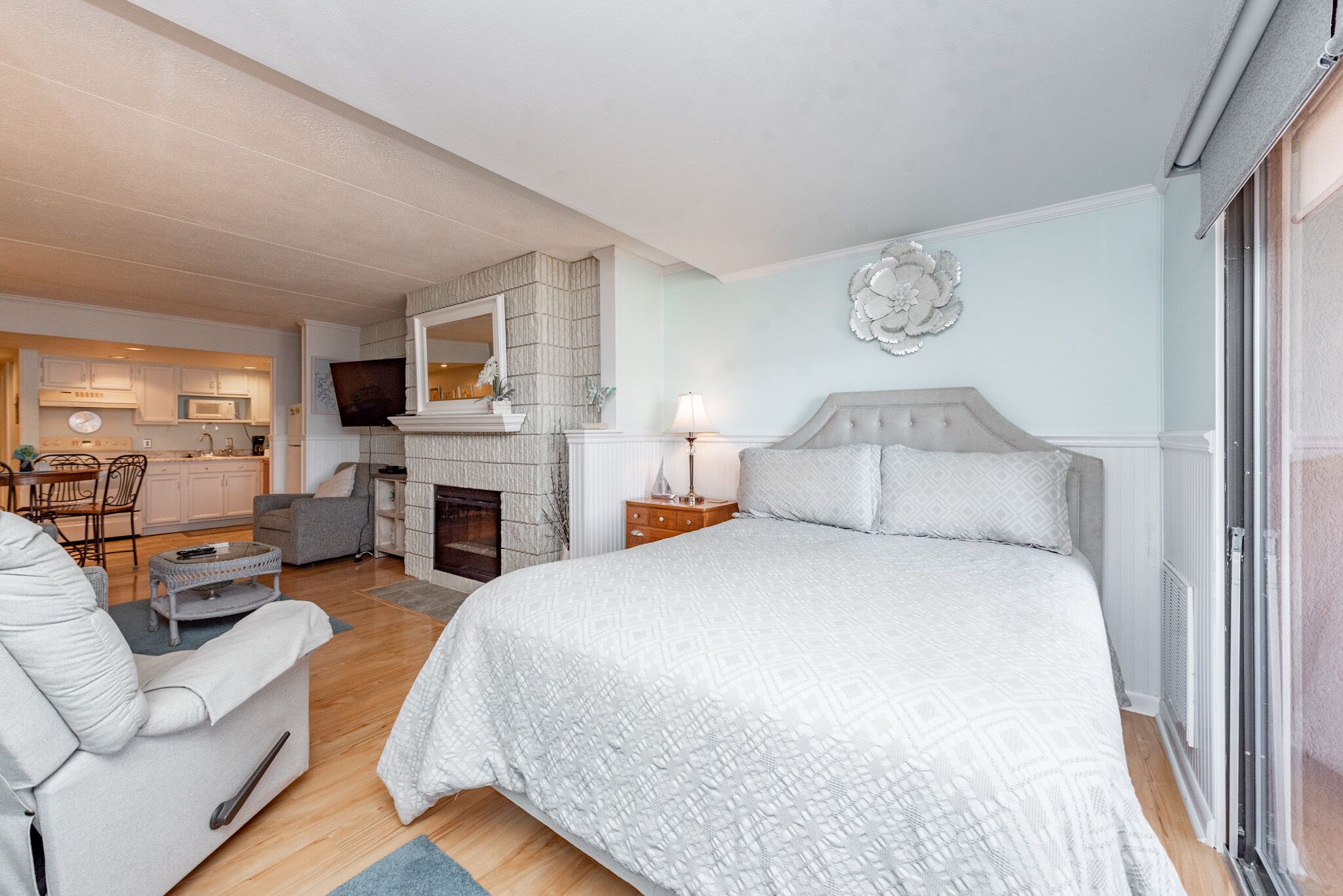 Una camera da letto con un letto grande, una zona salotto con una poltrona, un camino e una cucina sullo sfondo.