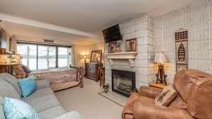 Ein gemütliches Wohnzimmer mit Kamin, einer Couch, einem Sessel und einem an der Wand befestigten Fernseher.