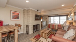 A living room with a fireplace, a television mounted above it, a sofa, a coffee table, and a dining area with chairs and a table.