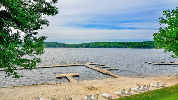 A lakeside view with a dock, sandy beach, and lounge chairs.