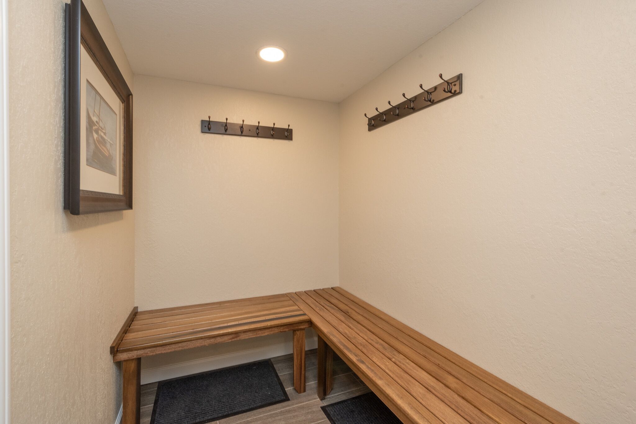 A corner room with a wooden bench, a coat rack, and a framed picture on the wall.