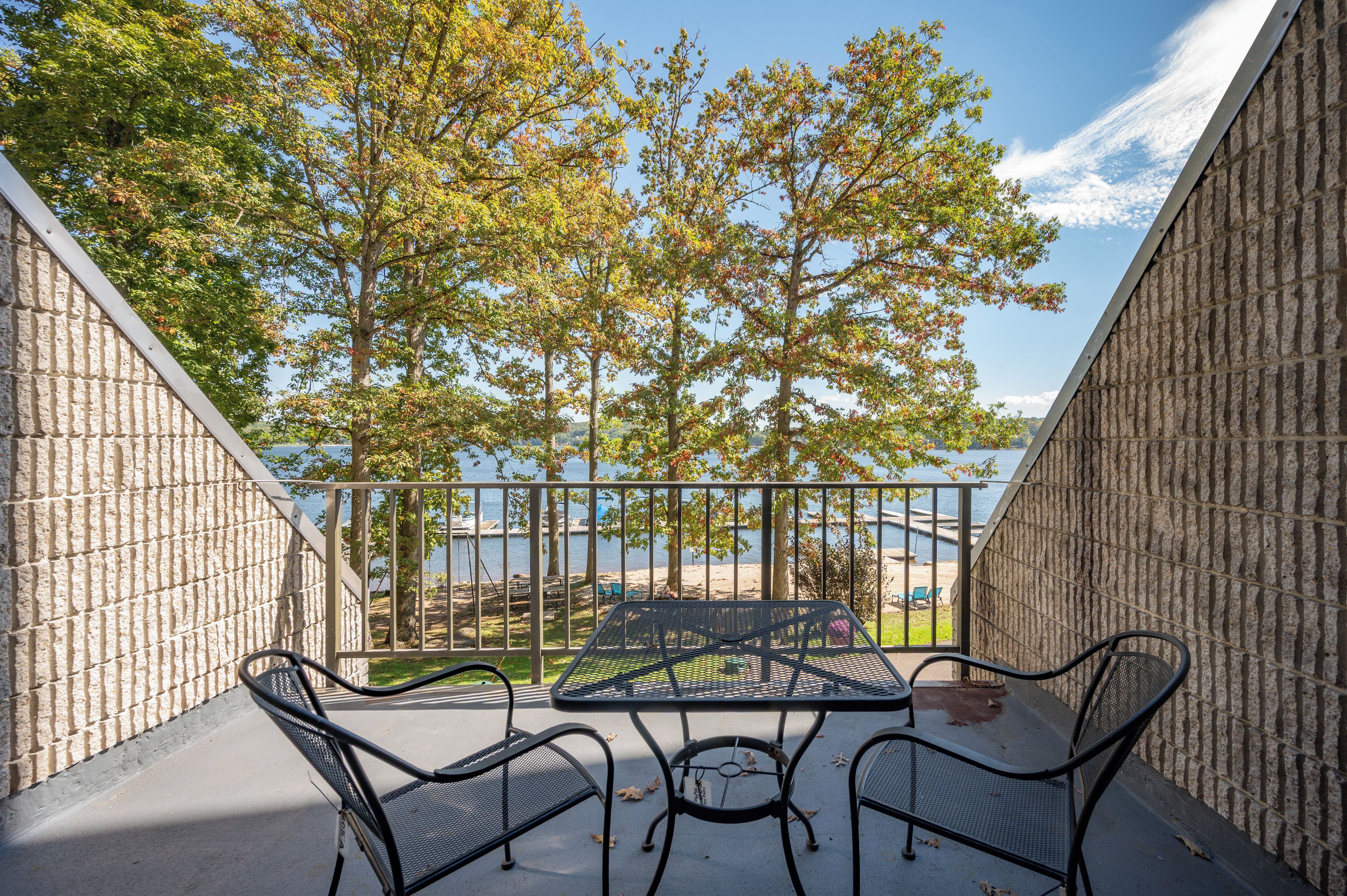 A balcony with a table and chairs, overlooking a body of water and trees.