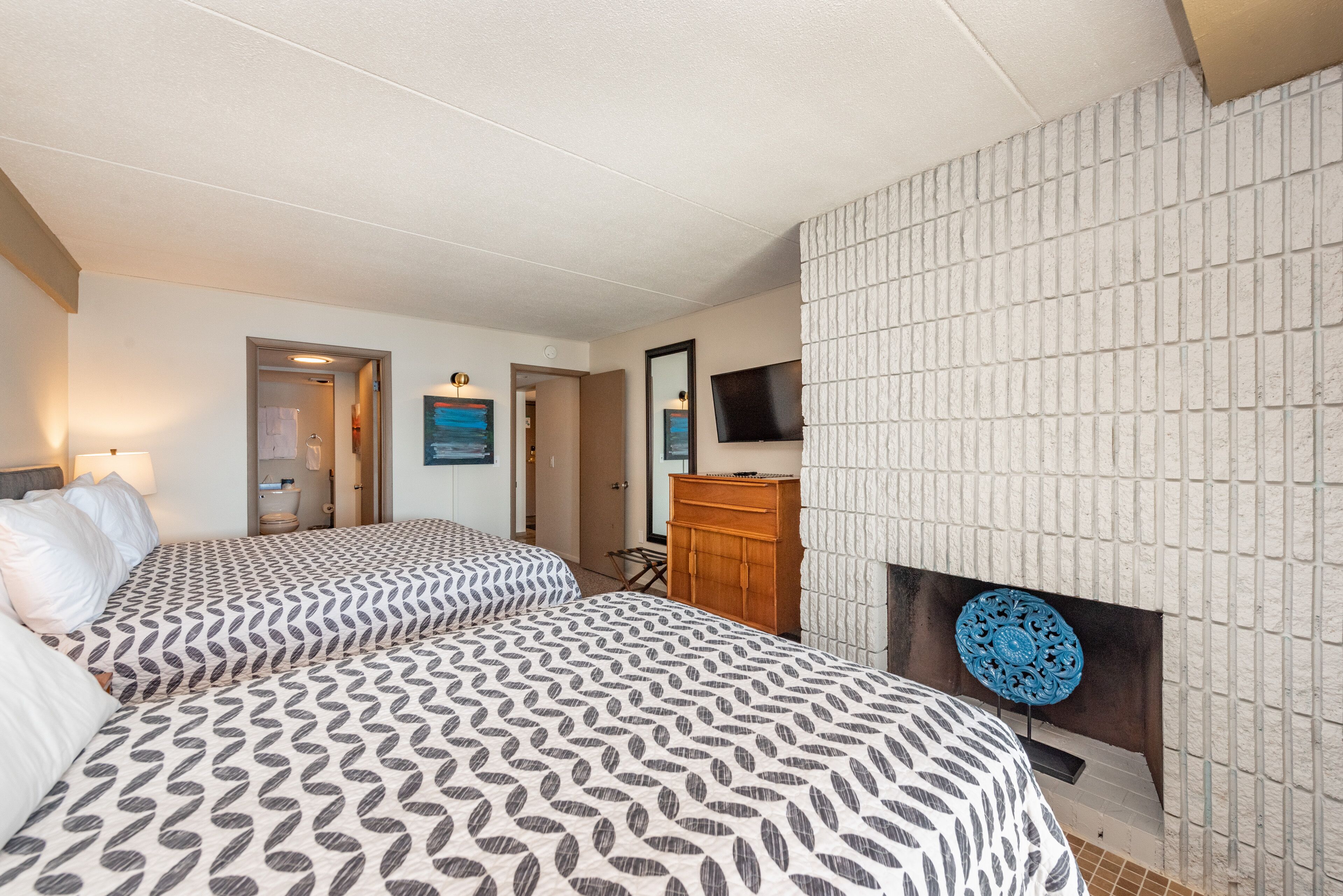 A hotel room with two beds, a wooden dresser, a flat-screen TV, and a decorative wall panel.