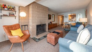 Een woonkamer met een open haard, een bruine leren fauteuil, een blauwe bank en een salontafel.