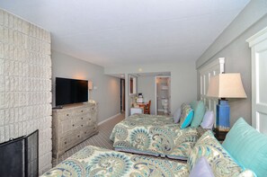 Habitación de hotel con televisión, cómoda, dos camas con ropa de cama estampada, lámpara y puerta que da a un baño.