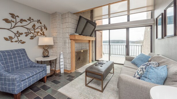 A modern living room with a fireplace, a sofa, a bench, and a view of the outdoors. - Will O' The Wisp: 301D Two Bedroom/Two Bath (Oakland)