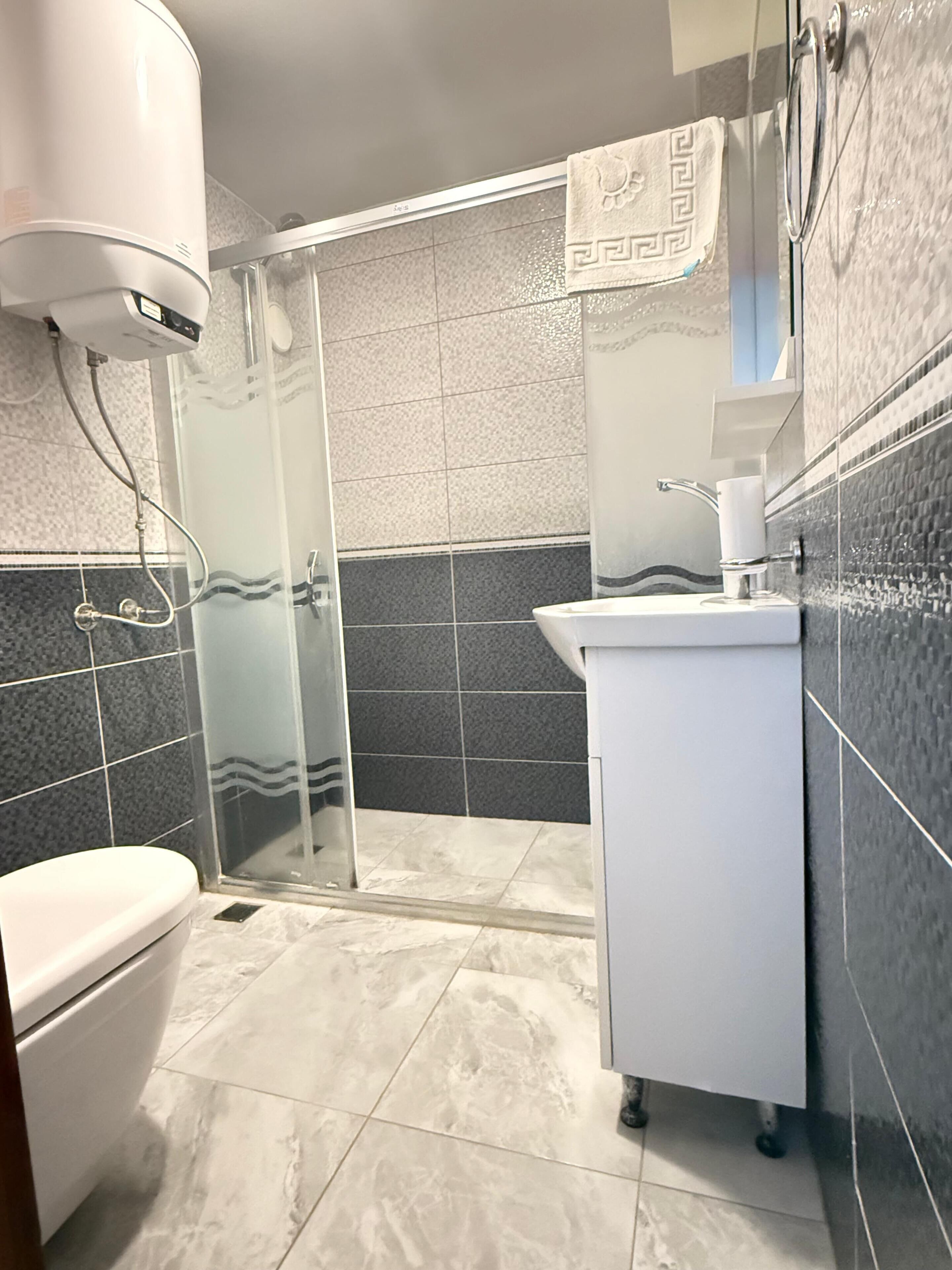 Une salle de bain avec une douche à parois de verre, des toilettes et un lavabo, avec une serviette accrochée au mur.