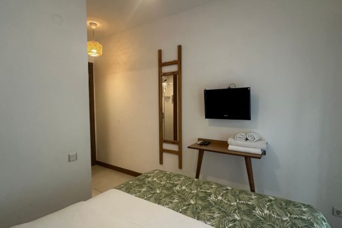Une chambre à coucher avec un lit, une télévision, un miroir et une petite table sur laquelle sont posées des serviettes.