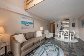 Un salon moderne comprenant un canapé, des fauteuils, une table basse en verre et un coin repas avec une table et des chaises.