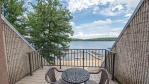 A balcony with a view of a lake, a table, and two chairs.