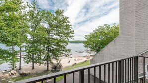 A view from a balcony overlooking a lake with trees, a sandy beach, and a dock.
