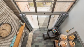 A high-ceilinged room with a large skylight, a clock, a sofa, and a small table with a decorative item.