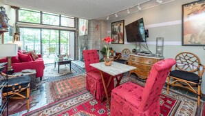 A spacious living room with a large window, a red sofa, a wooden table, and a television.