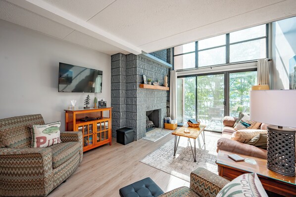 Una sala de estar moderna con chimenea, sofá, televisor y ventanas amplias.