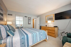 Un dormitorio con cama, cómoda, televisor y una puerta que da a otra habitación.