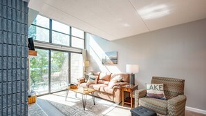 A modern living room with a sofa, armchair, coffee table, and a view through large windows. - Will O' The Wisp: 308D Two Bedroom/Two Bath (Oakland)