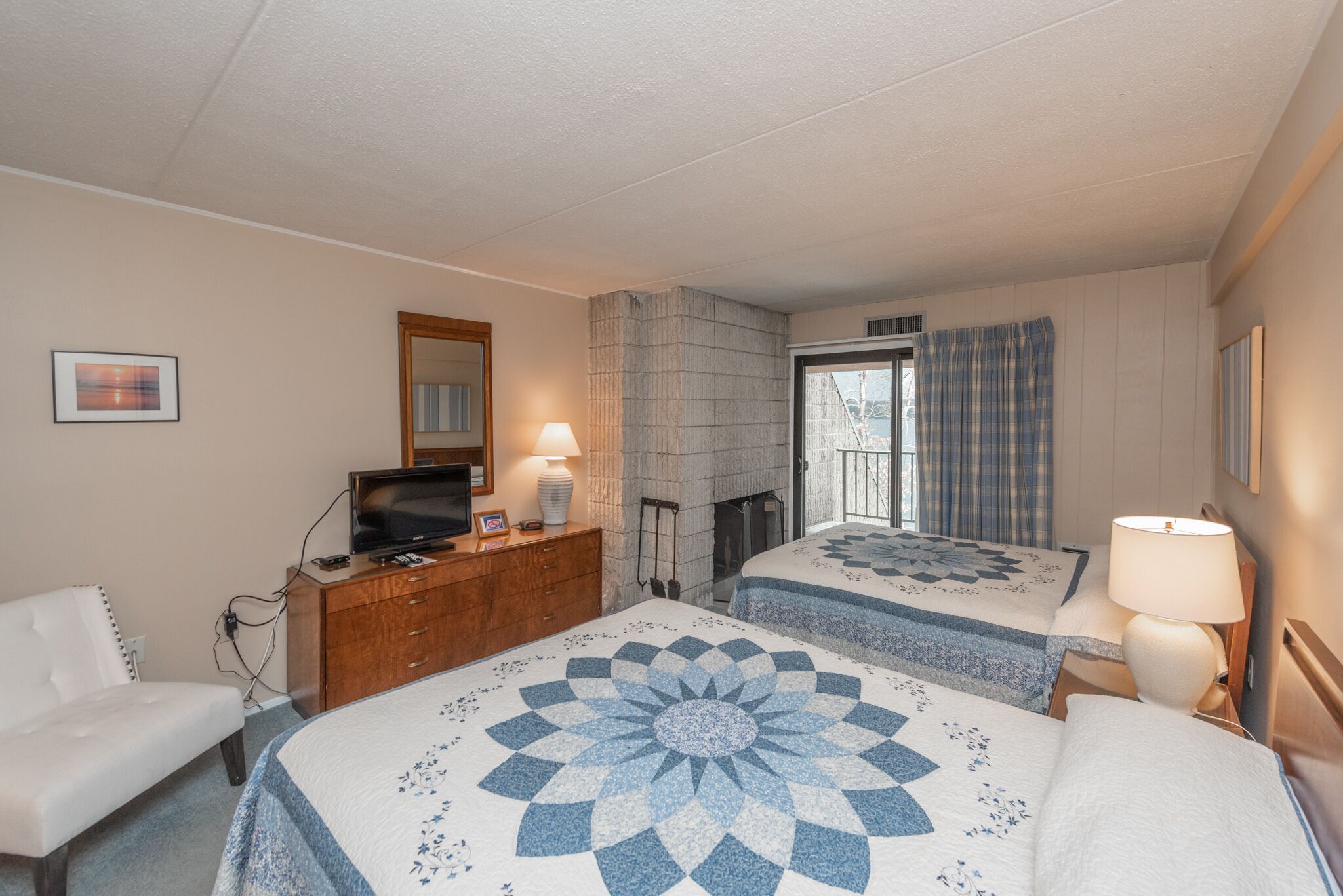 Una camera d'albergo con due letti, una televisione su un comò, un camino e una finestra con tende.