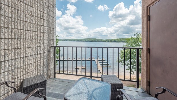 Un balcón con mobiliario de mimbre, una mesa de cristal y vistas a un lago con muelles.