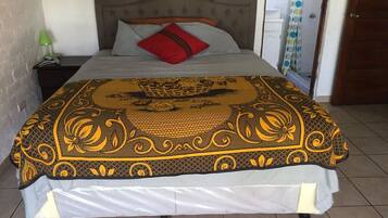 Un lit avec une couvre-lit à motifs, une tête de lit grise et un oreiller rouge.